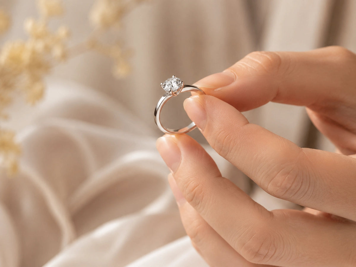 Hand holding a diamond ring by the metal band, showing a careful way to handle 18K gold and lab-grown diamond jewelry.