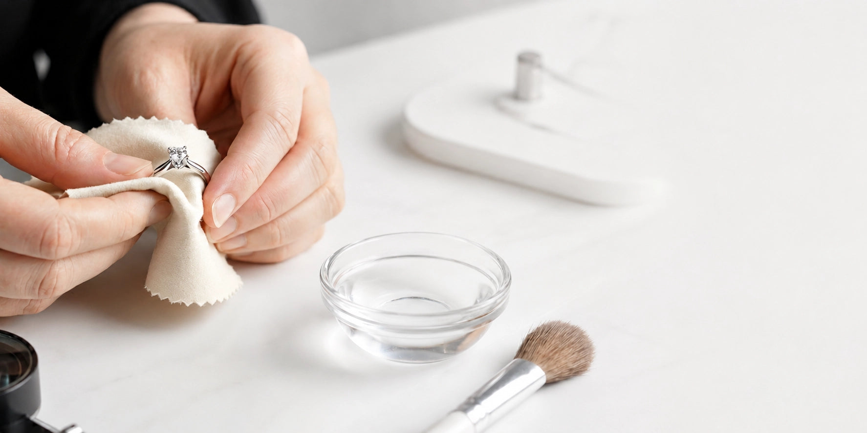 Hands gently cleaning a diamond ring with a soft cloth, representing J'ENCHANTE jewelry care for 18K gold and lab-grown diamond pieces.