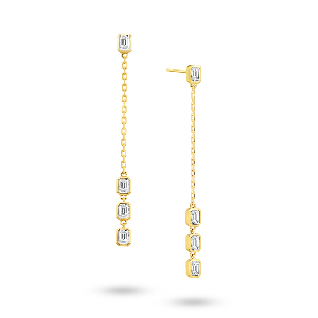 Angled view of the J'ENCHANTE DEW 50mm emerald-cut diamond drop earrings. The image highlights the delicate gold chain and the sharp, composed facets of the step-cut diamonds. Balanced between precision and movement, this refined design offers graphic brilliance ideal for confident workwear or minimalist evening styling.