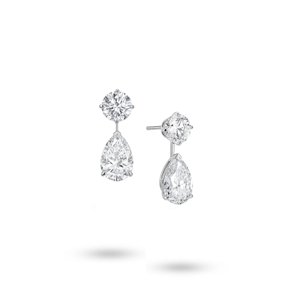 Angled view of the J'ENCHANTE The Dualis diamond drop earrings, showcasing the refined 18K white gold setting and secure earring posts. This perspective highlights the virtually invisible connection between the round and pear-shaped diamonds, illustrating a sophisticated "less reveals more" approach that allows each stone to stand and shine independently.