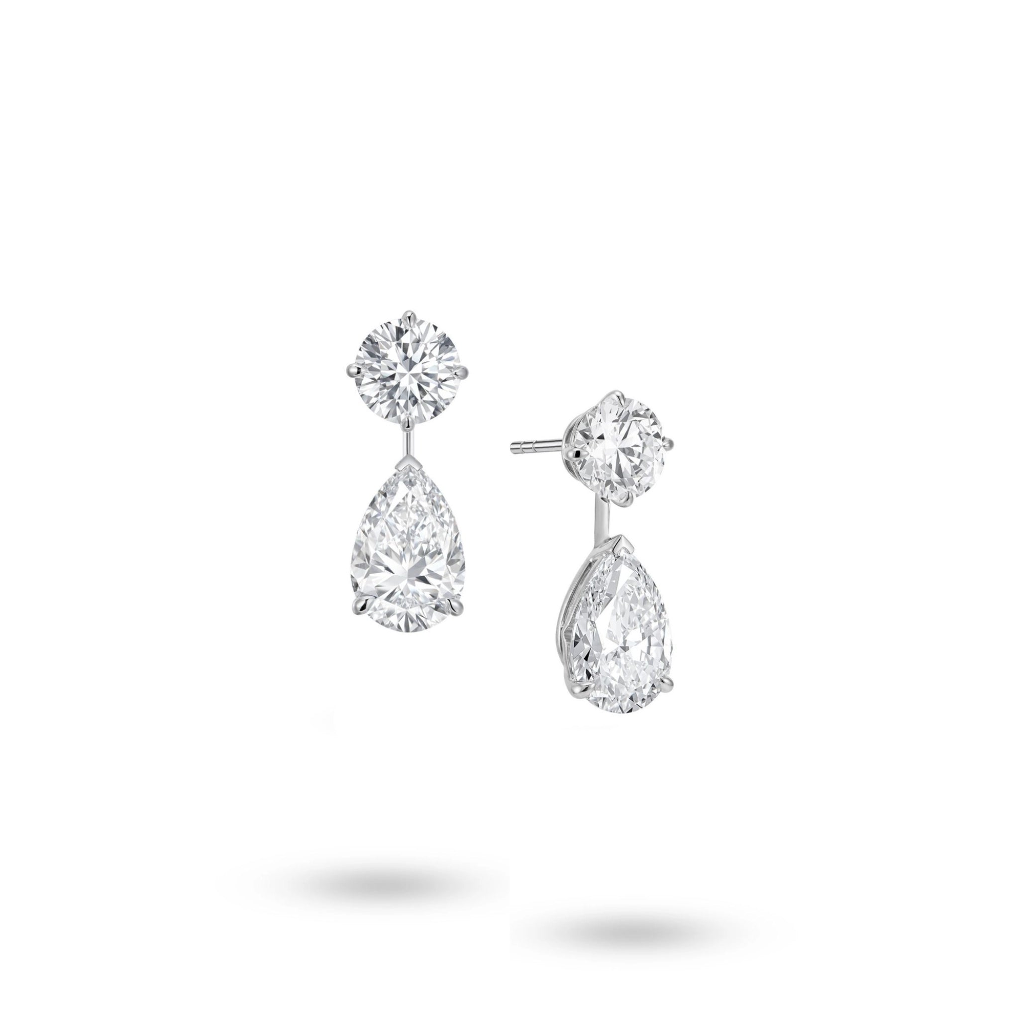 Angled view of the J'ENCHANTE The Dualis diamond drop earrings, showcasing the refined 18K white gold setting and secure earring posts. This perspective highlights the virtually invisible connection between the round and pear-shaped diamonds, illustrating a sophisticated "less reveals more" approach that allows each stone to stand and shine independently.