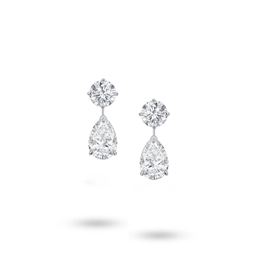 Front view of the J'ENCHANTE The Dualis drop earrings in 18K white gold. Defined by a pure expression of duality, each earring pairs a precise round brilliant diamond with a gracefully suspended pear-shaped drop (4 diamonds totaling approx. 6.1 carats). The minimal connection enhances a sense of lightness, capturing the perfect balance between strength and softness in its purest form.