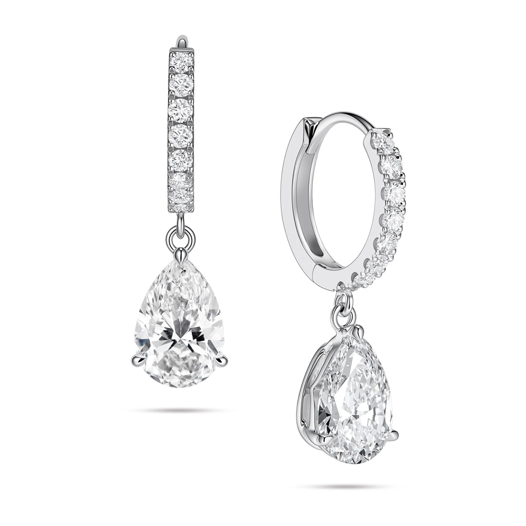 Angled view of the J'ENCHANTE JOY pear drop earrings in 18K white gold. The image showcases a pair of slim pavé hoops and graceful pear-shaped drops, with one earring highlighting the signature J-shaped side profile designed to securely support the diamond while maximizing side light entry for enhanced dimension.