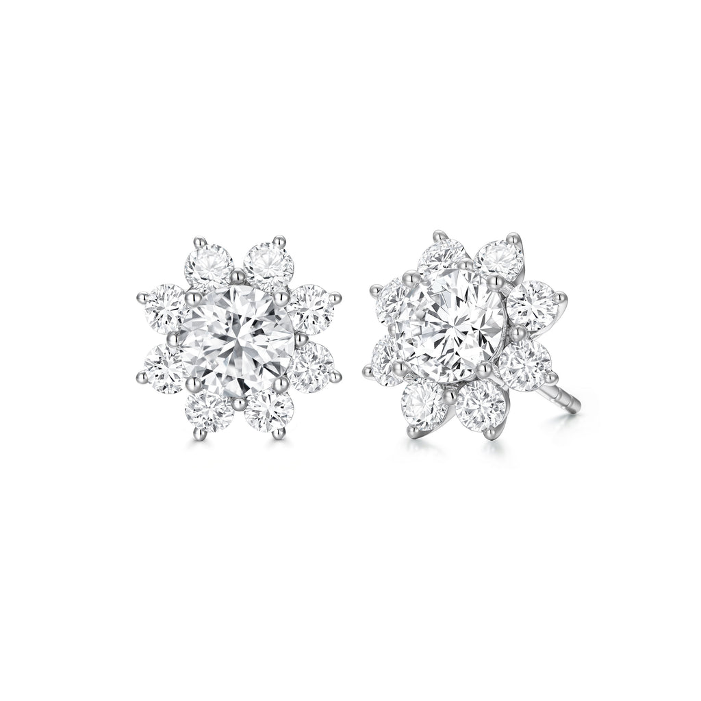 Angled view of the J'ENCHANTE LIFE Bloom diamond stud earrings in white gold. Inspired by a sunflower silhouette, each earring features a luminous center diamond framed by a radiant halo of 16 round stones (approx. 0.88 carats). The refined layered setting amplifies light and dimension, naturally drawing the eye to the brilliant core.