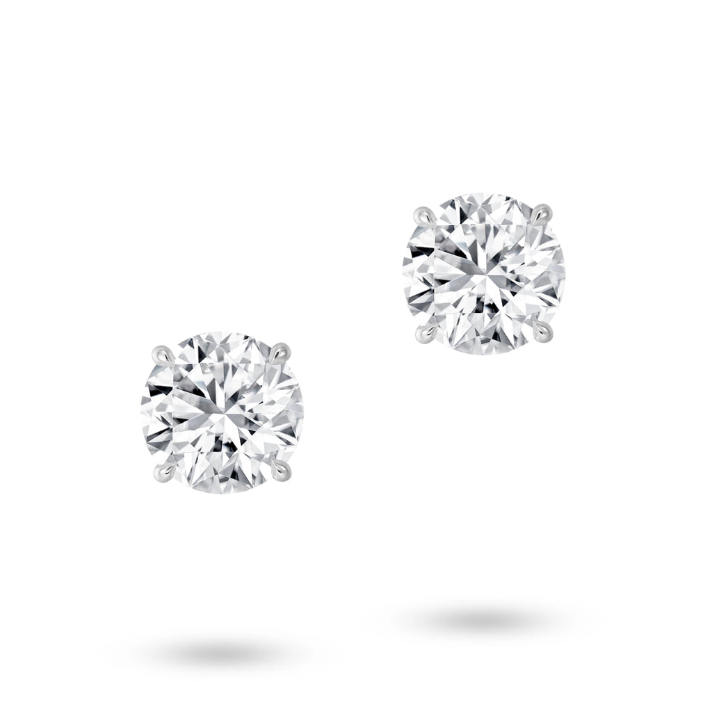 Front view of the J'ENCHANTE ONE round cut diamond stud earrings, featuring a magnificent 2-carat brilliant round diamond on each ear. Free from embellishment, the minimalist white gold design expresses the purest relationship between form and light.